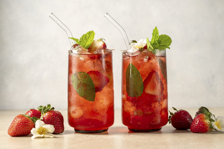 Refreshing strawberry summer drink in glass with ice cubes and mint leaves.